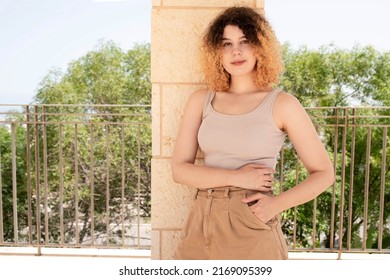 Young Woman With Curly Dyed Hair Smiling While Standing Outside. Confident Teenager Girl With Beautiful Figure. Eye Contact. Sunny Day. Concept Of Women's Health, The Effect Of The Sun On The Skin.