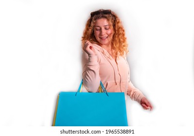 Young woman with curly hair, blue jeans and rose hoodie carries a blue shopping bag.