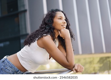 A young woman with curly hair gazes thoughtfully into the distance, leaning against a shiny railing in a vibrant outdoor setting filled with lush greenery and vivid colors, enjoying the moment - Powered by Shutterstock