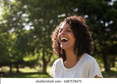 Junge Frau mit lockigen Haaren lachen, während sie draußen in einem Park auf einem sonnigen Sommernachmittag steht