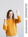 Young woman with curly hair, raising fists in excitement. She looks overjoyed and triumphant, celebrating a win. Isolated against a white background, perfect for themes of success and happiness.