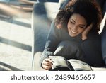 Young woman with curly hair relaxes on her couch, reading a magazine in her cozy living room, enjoying a carefree day at home