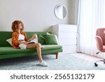 A young woman with curly hair relaxing on a green sofa in a cozy living room, wearing casual summer clothing and enjoying a book, with sunlight streaming in through large windows