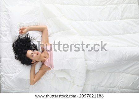 Young woman with curly hair sleeping in white bed top view