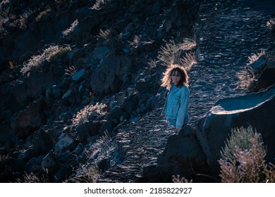 Young Woman With Curly Hair Trekking On A Rock Path In Sunset Light