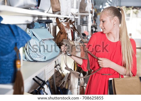 Young woman customer is choosing new modern hand bag in boutique
