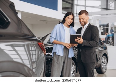 Young woman customer female buyer client wears shirt consult with salesman hold tablet choosing auto want to buy new automobile in car showroom vehicle salon dealership store motor show. - Powered by Shutterstock