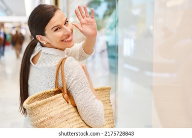 Young woman as a customer waves happily while shopping in the shopping arcade