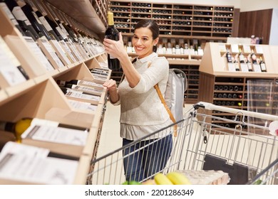 Young Woman As A Customer And Wine Connoisseur With A Bottle Of Wine In A Wine Shop Or Supermarket