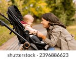 Young woman with a cute baby girl in baby stroller at the autumn park