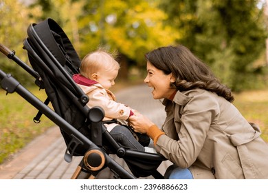 Young woman with a cute baby girl in baby stroller at the autumn park