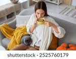 Young woman with cute British cat drinking green tea at home on autumn day