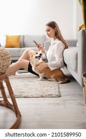 Young Woman With Cute Corgi Dog Using Mobile Phone At Home