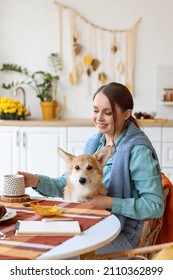 Young Woman With Cute Corgi Dog And Cup Of Tea Sitting At Table In Kitchen