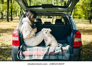 Young woman and cute dog relaxing enjoying happy moment in the forest sitting in car trunk. Vacation, holidays, travel,  adventure - Powered by Shutterstock