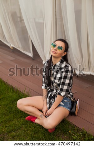 Young woman with cute hairstyle is sitting on a wooden floor near a 
curtain in pink shoes on the background of green nature.