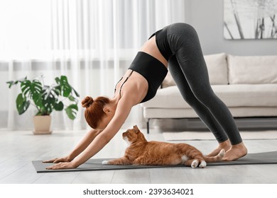 Young woman with cute red cat practicing yoga on mat at home - Powered by Shutterstock