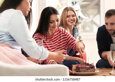 Young Woman Cutting Birthday Cake And Her Friends At Party Indoors