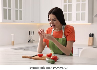 Young woman cutting finger with knife while cooking in kitchen