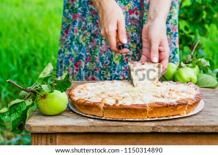Young woman cutting fresh summer apple pie with almond flakes and sugar powder. Outdoor picnic background