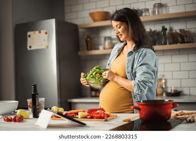 Young woman cutting vegetables in kitchen. Beautiful pregnant woman making salad - Powered by Shutterstock