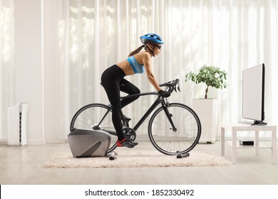 Young Woman Cycling With Stationary Bicycle Trainer At Home In Front Of Tv