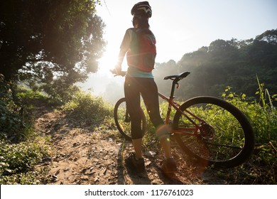 Young woman cyclist carrying mountain bike on summer forest trail - Shutterstock ID 1176761023