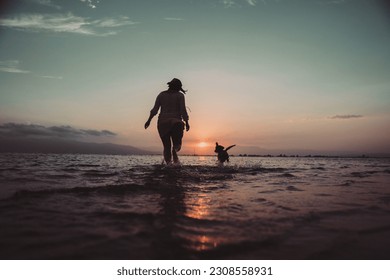 Young woman and dachshund dog run at sunset on the beach shore