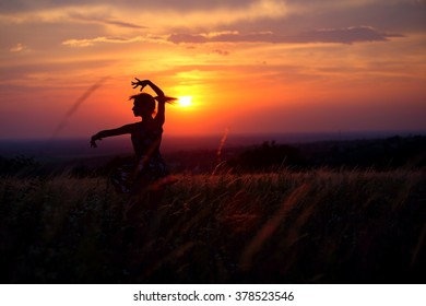 Young woman dancing alone in a field during sunset. Dancing silhouette of a young girl with sunset background.