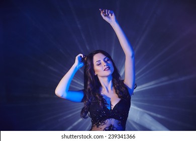 Young woman dancing in club with light rays on background