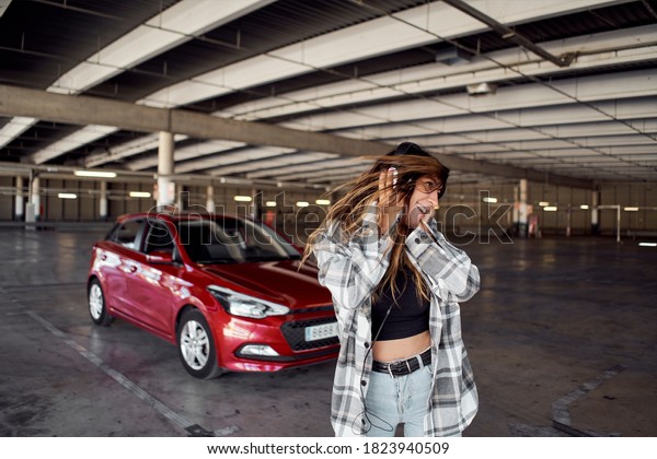 Young woman dancing in a parking lot. She is\
listening to music with\
headphones.