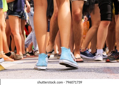 Young Woman Is Dancing In Street Party. Carnaval. Camera Low Angle, Many Anonymous Legs In A Crowd. All People Wear Shorts. Summer. Outdoor Party, Movement, Fun, Relaxation.