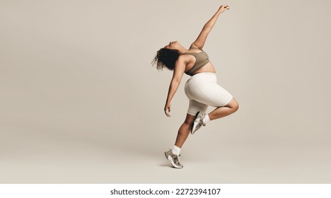 Young woman dancing in a studio, wearing fitness clothing. Young female expressing her self-assurance and body confidence, effortlessly finding her flow in a body movement.
