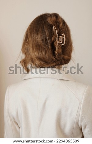 Young woman with dark blonde hair in a winter white coat. Claw clip hairstyle. Gold metal claw clip. Trendy hairstyle. Elegant hairstyle. Messy hairstyle. 