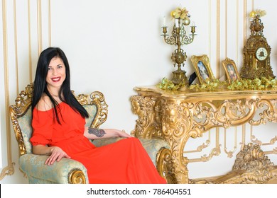 Young Woman With Dark Hair In A Long Red Dress In A Baroque, Renaissance Or Rococo Living Room. In A Luxurious Interior