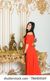 Young Woman With Dark Hair In A Long Red Dress In A Baroque, Renaissance Or Rococo Living Room. In A Luxurious Interior