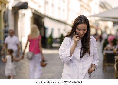 Young woman with dark long hair talking on phone walking through the street.