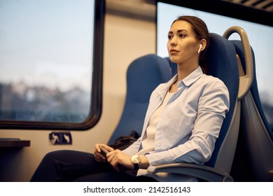 Young Woman Day Dreaming And Listening Music Over Earbuds While Commuting By Train.