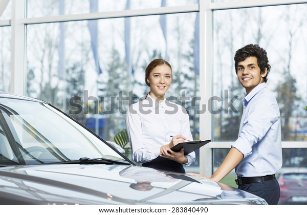 Young woman dealer in auto salon presenting car\
to customer