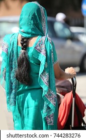 Young Woman With Decorated Dress And Long Black Hair Braid Coming Out Of The Veil While Pushing A Stroller To The City