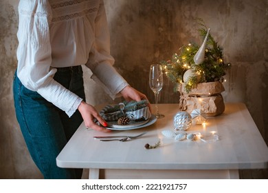 young woman decorates and sets a festive Christmas table with a spruce composition, Christmas and New Year dinner