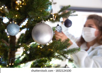 Young woman decorating a Christmas tree with medical safety mask for Covid-19, Coronavirus and Christmas concept, beautiful holiday background - Powered by Shutterstock