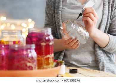 Young woman decorating DIY jars with paint