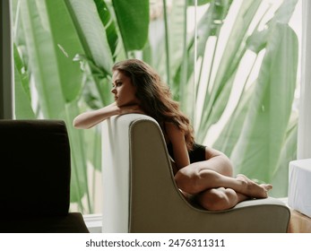 Young woman in deep thought lounging on a modern chair by large tropical leaves - Powered by Shutterstock