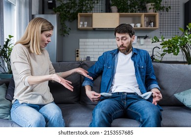 A young woman demands money from her husband, the man does not show empty pockets. At home, sitting on the couch. Quarrels, conflicts, misunderstandings. Money crisis - Shutterstock ID 2153557685