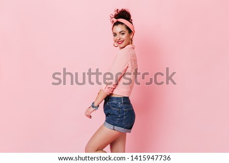 Young woman in denim shorts, pink blouse and headband cute smiling on isolated background