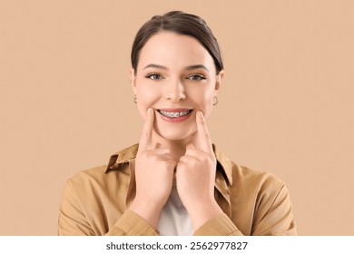 Young woman with dental braces smiling on beige background