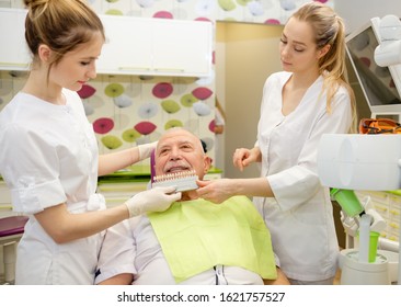 Young Woman Dentist Looking Whether Ceramic Veneer Fits Tooth Of Elderly Man 70-75 Years Old Sitting In Dental Chair In Stomatology Clinic. Concept Of Dentistry, Medicine And Health Care