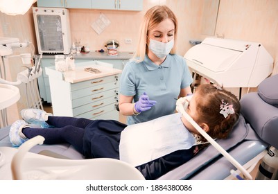 Young woman dentist in medical face mask holding dental instruments while little girl lying in dental chair with inhalation sedation. Concept of sedation dentistry. - Shutterstock ID 1884380086
