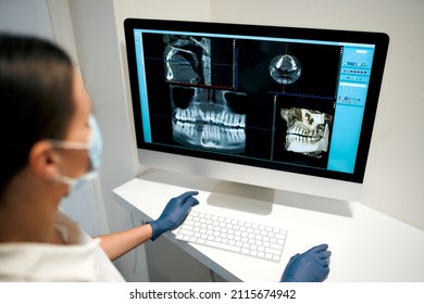 A young woman dentist in a medical mask examines an x-ray image on a computer in a dental office with modern equipment. Caries treatment. Dentistry and dental care.
